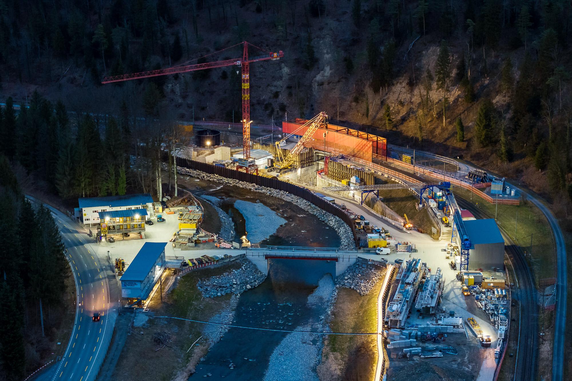Eine grosse Baustelle befindet sich am Sihlufer mit Bürogebäuden, einem Raupenkran, einem Baukran, einem Förderband und einem weiteren Baustellengebäude. Es ist Nacht.