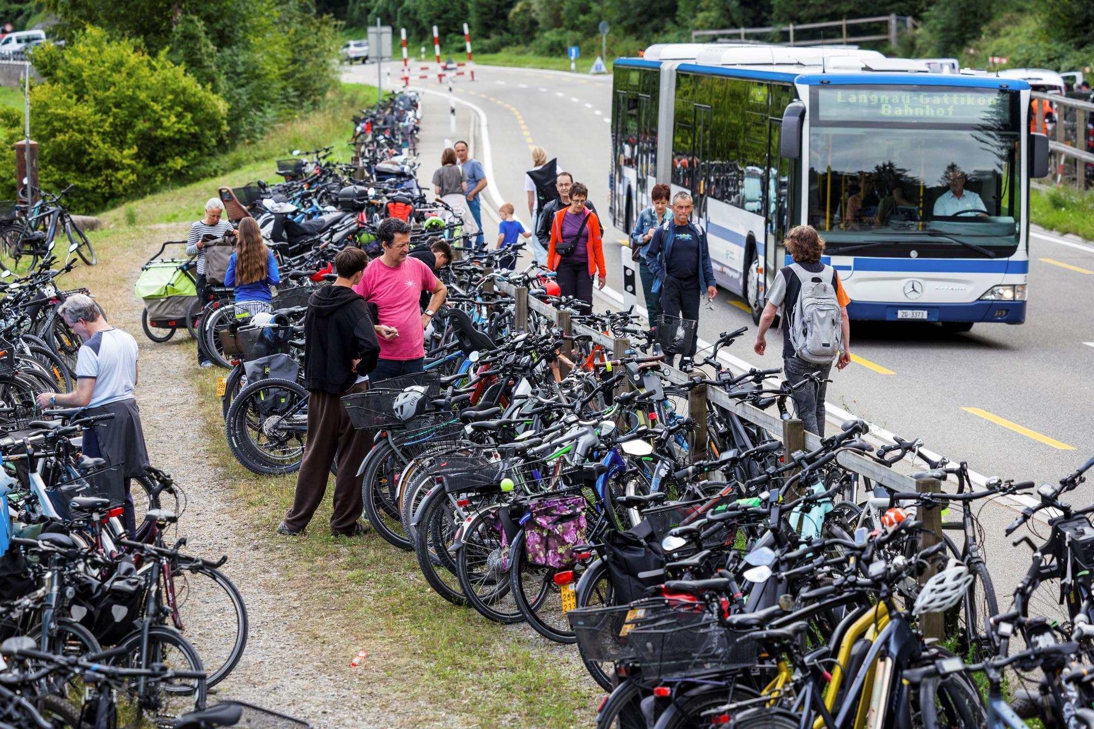 Zahlreiche parkierte Fahrräder am Strassenrand, ankommende Leute und ein Bus, der vorbeifährt.