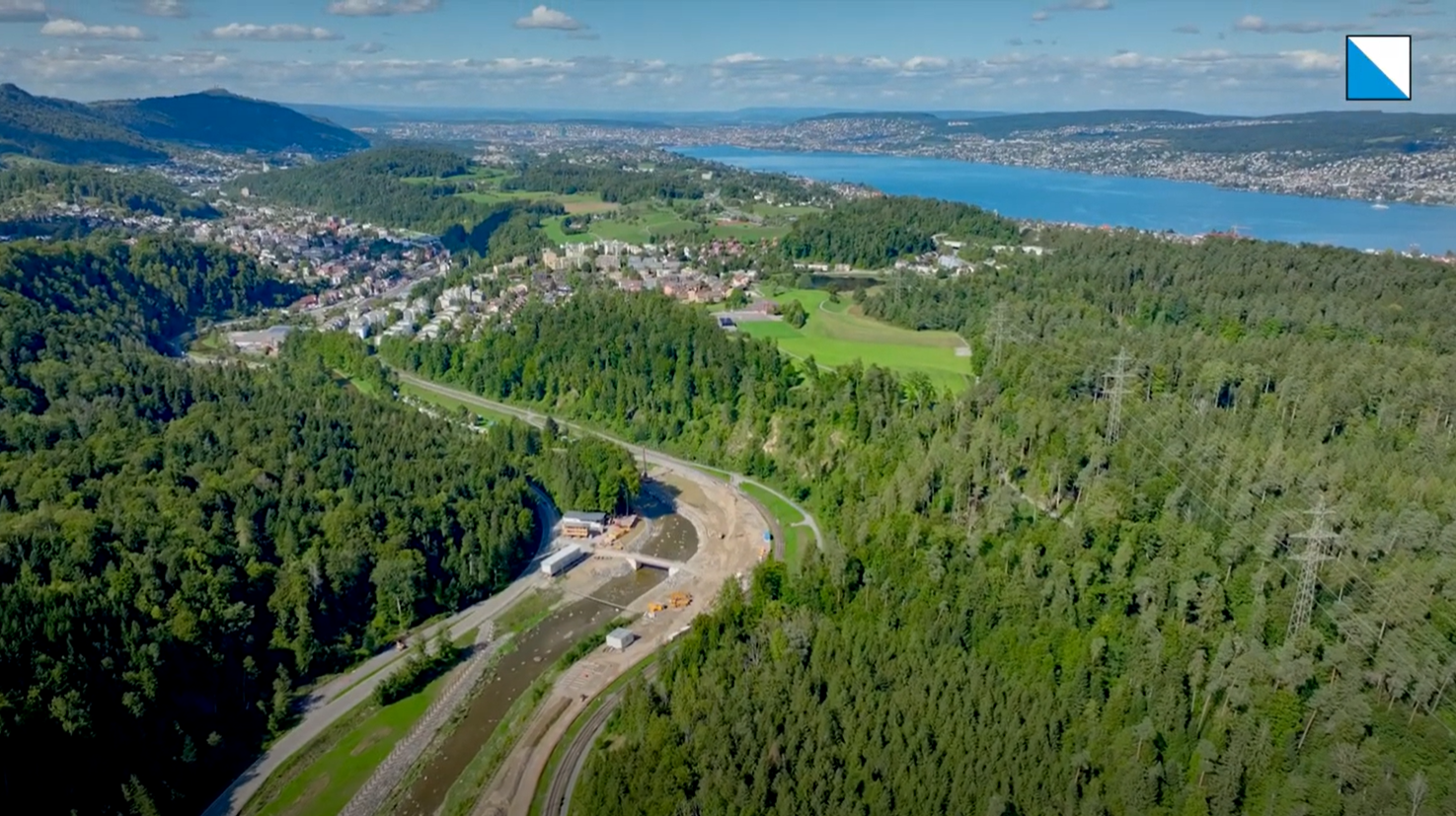 Luftaufnahme des Sihl-Tals mit Bauarbeiten am Fluss, umgeben von Wald, einem Dorf und dem Zürichsee im Hintergrund.