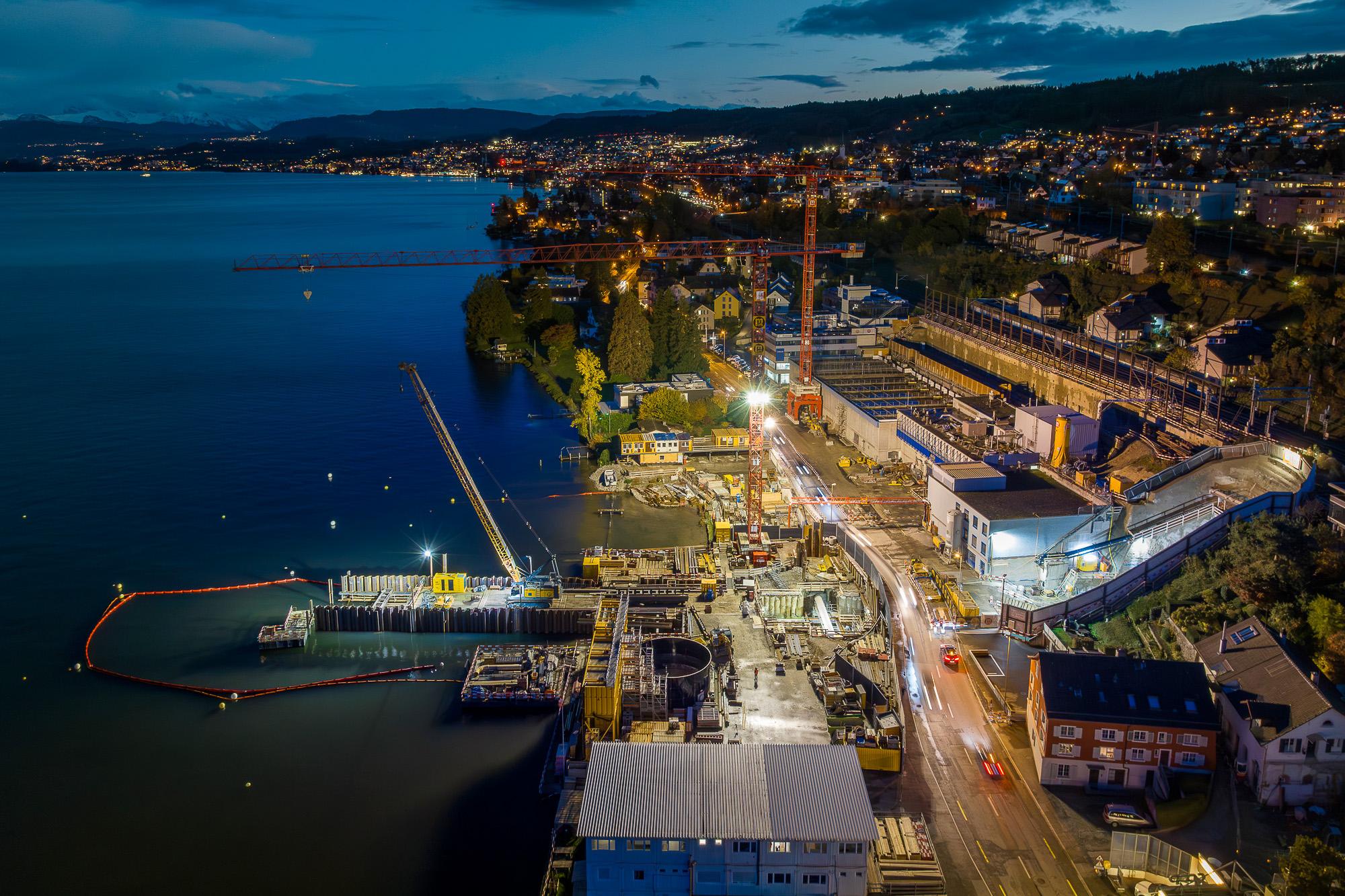 Luftaufnahme des Zürichseeufers in Thalwil in der Dämmerung. Links ist der See, auf der rechten Seite befindet sich das Ufer mit einer grossen Baustelle
