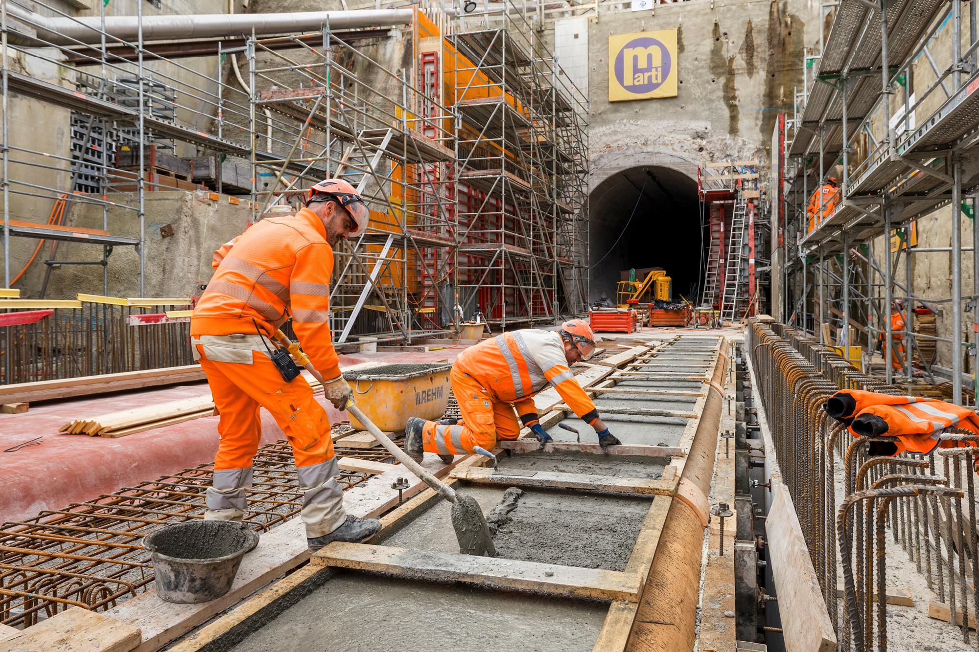 Stollenausgang, davor Baurarbeiter bei Betonarbeiten von Hand umgeben von Baugerüsten