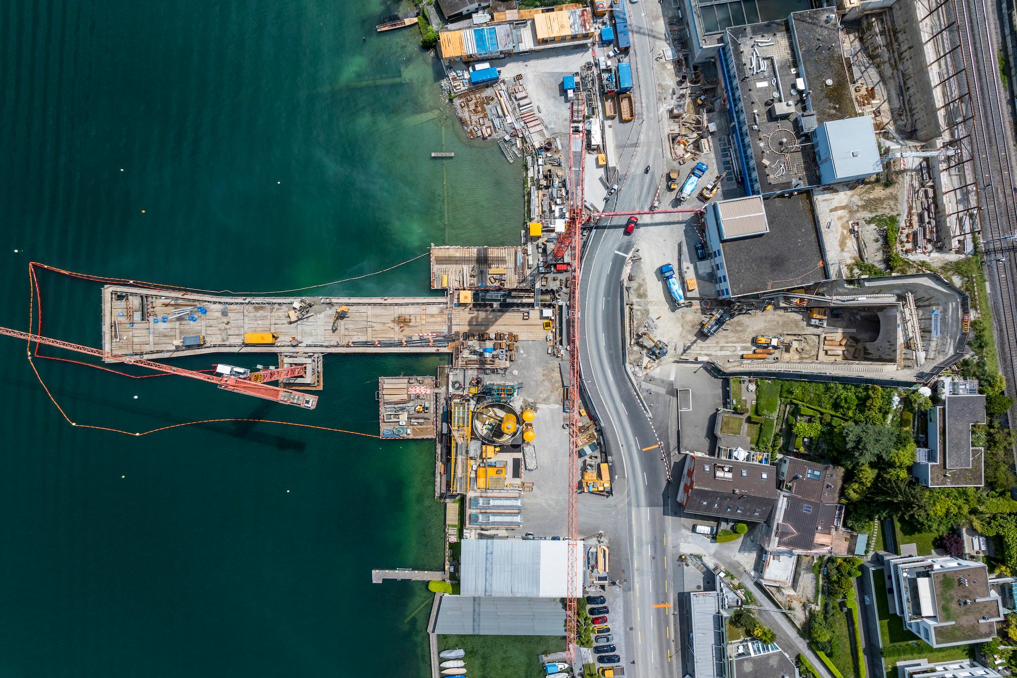 Luftaufnahme der Baustelle des Auslaufbauwerks. Auf der linken Seite liegt der See, auf der rechten Seite das Seeufer mit einer grossen Baustelle. 