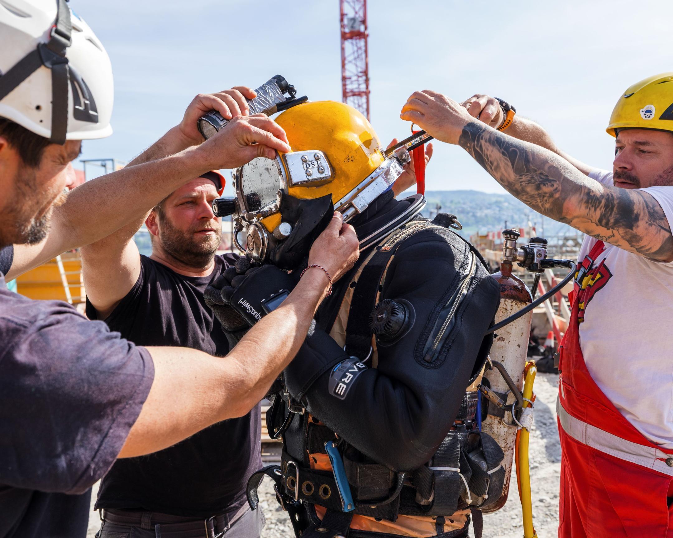 Ein Taucher wird mit Hilfe von drei Personen für seinen Einsatz vorbereitet.