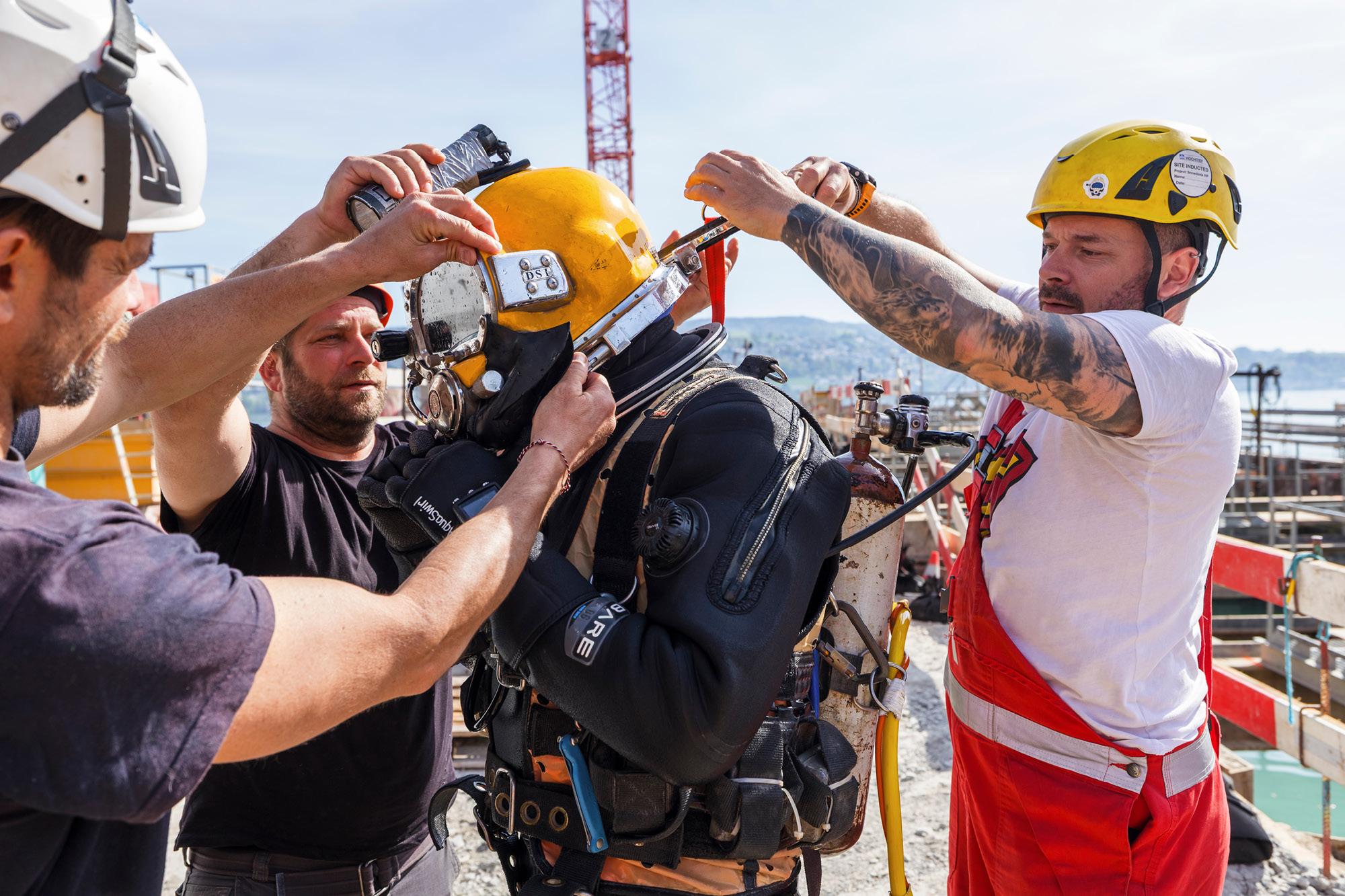 Ein Taucher wird mit Hilfe von drei Personen für seinen Einsatz vorbereitet.