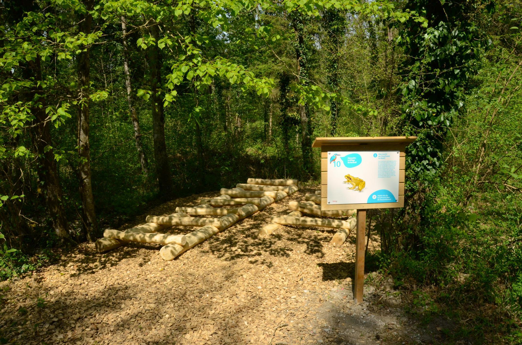 Neue Beschilderung für Posten Zehn und übereinandergelegte Holzbalken wie Treppe im Hintergrund für Froschhüpfen.