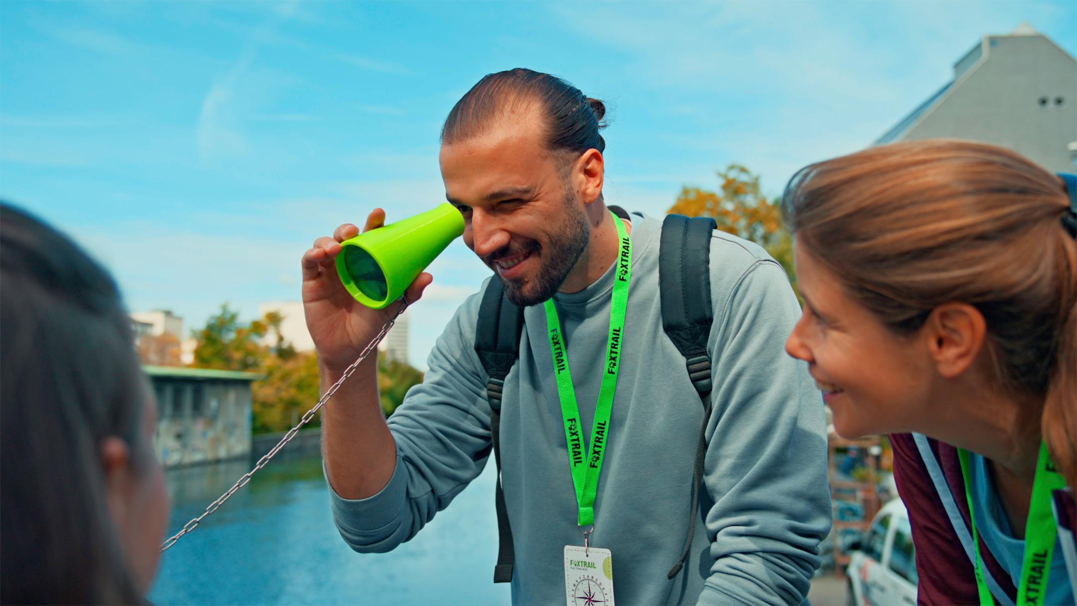 Ein Foxtrail-Teilnehmer schaut durch ein Fernrohr, zwei Mitspielerinnen schauen ihm zu