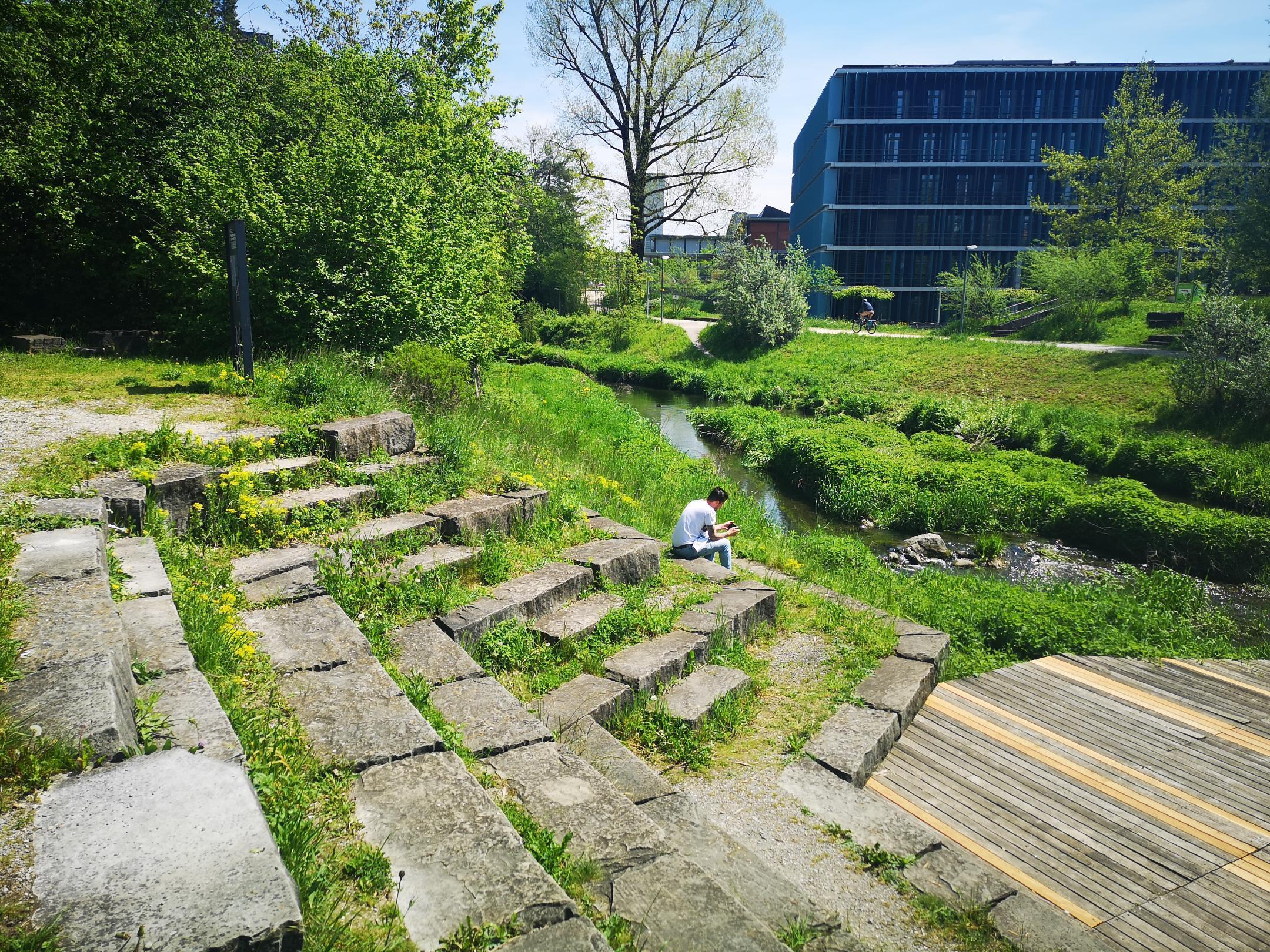 Der Chriesbach schlängelt sich vor der EAWAG in Dübendorf durch das Grün. Im Bild links sind natürliche Sitzstufen angebracht, die eine Art Arena bilden.