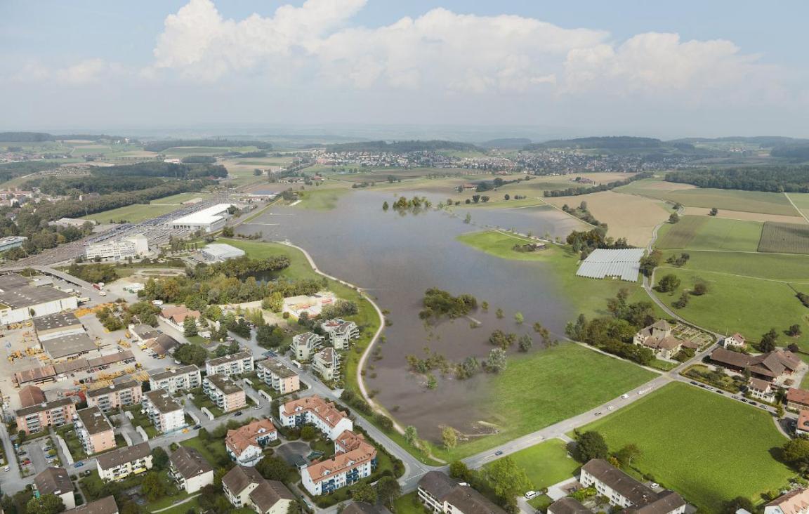 Die Visualisierung zeigt eine Luftaufnahme des Rückhalteraums Hegmatten bei Hochwasser.  Die grosse Wiese neben der Wohnsiedlung steht unter Wasser.