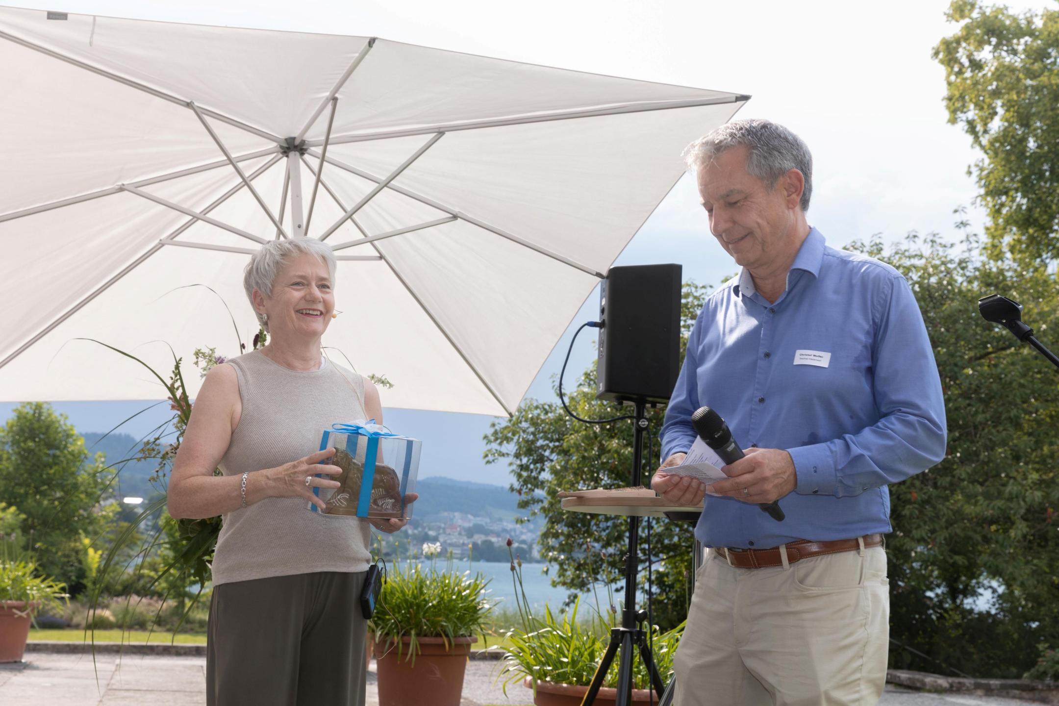 Eine Frau und ein Mann vor einem Sonnenschirm, sie übergibt ihm ein Geschenk.