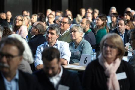 Viele Menschen sitzen an Tischen und schauen in eine Richtung.