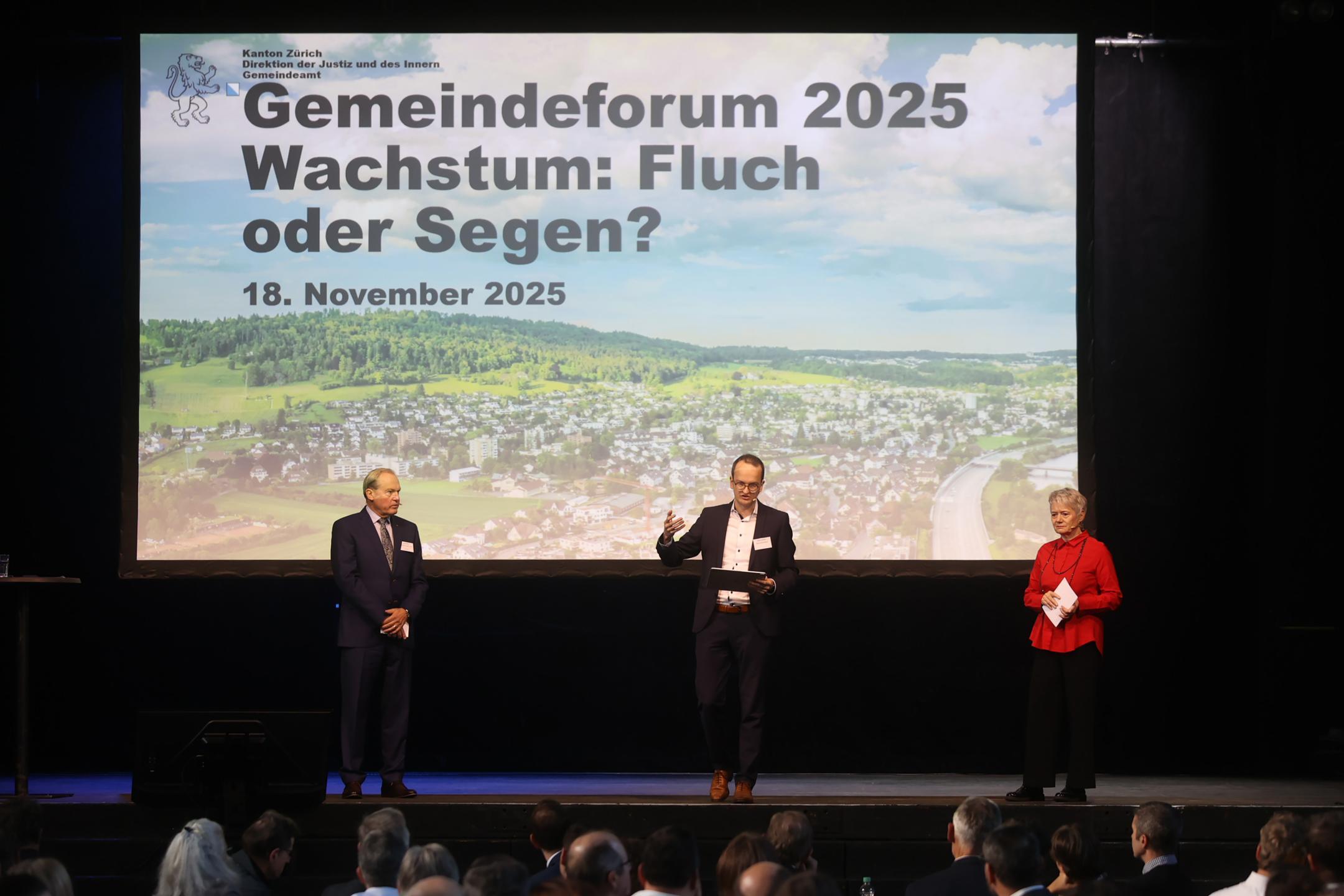 Drei Menschen stehen auf einer Bühne, im Hintergrund eine Leinwand mit dem Schriftzug «Gemeindeforum 2025 - Wachstum: Fluch oder Segen?»