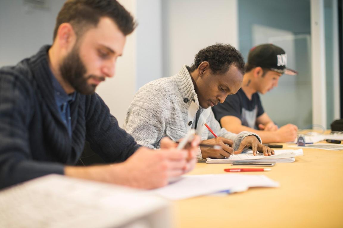 Drei Männer sitzen an einem langen Tisch und sind in theoretische Arbeiten vertieft.