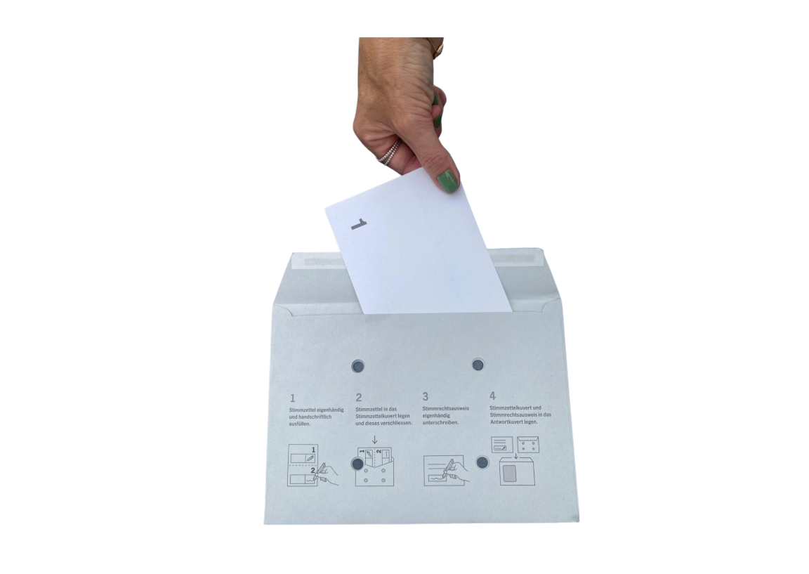 Eine Hand steck einen Stimmzettel ins Stimmkuvert
