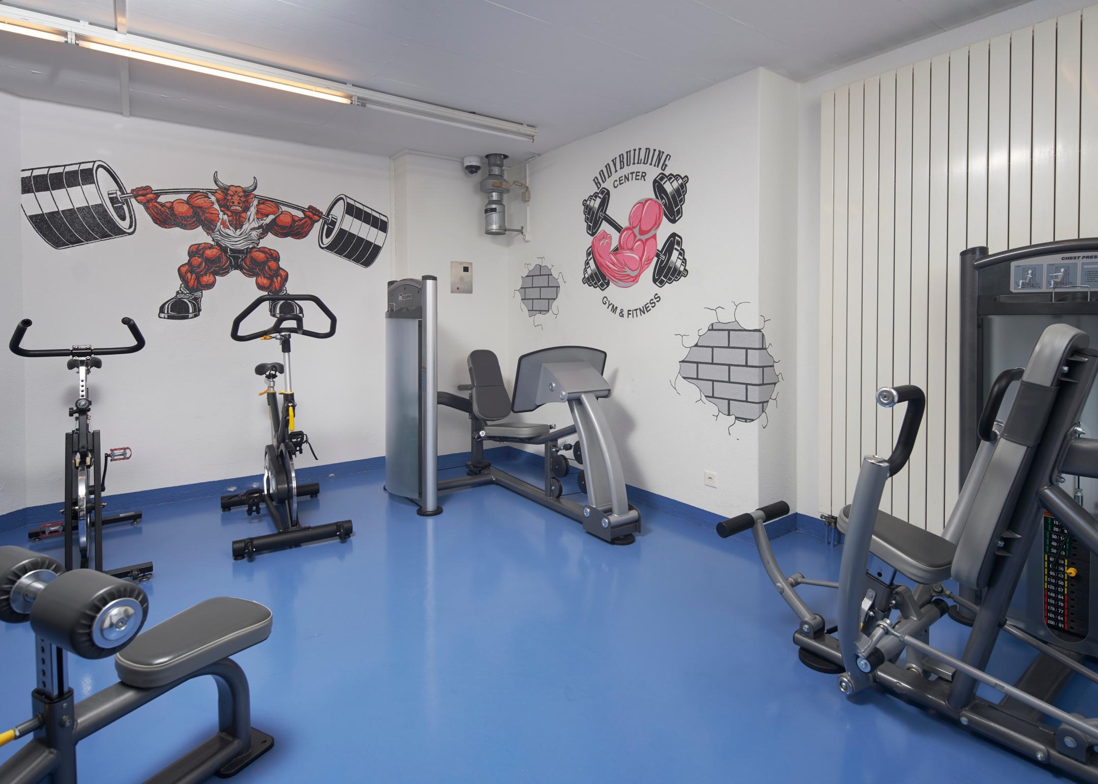 Fitnesstaum mit verschiedenen Sportgeräten und Graffitis an der Wand.