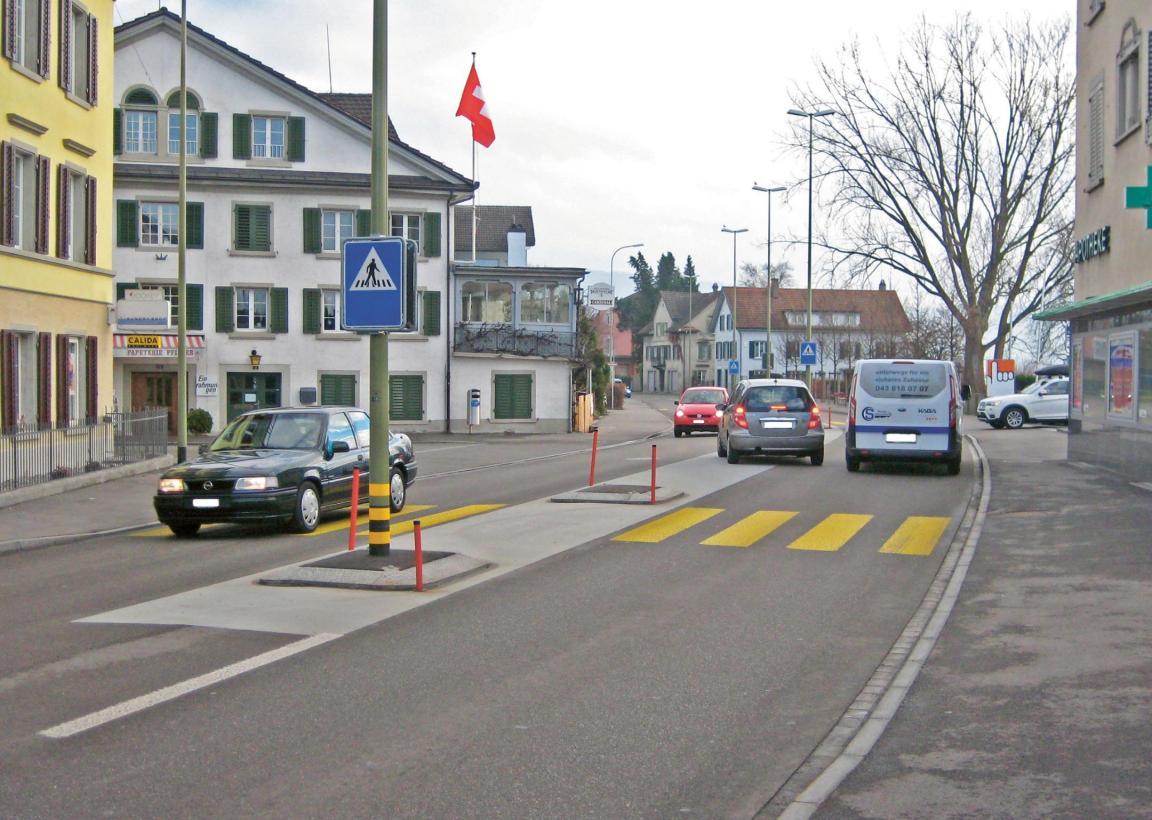 Übersichtsaufnahme eines Strassenabschnittes, ein Fahrzeug wartet auf dem Mehrzweckstreifen bis es nach links abbiegen kann