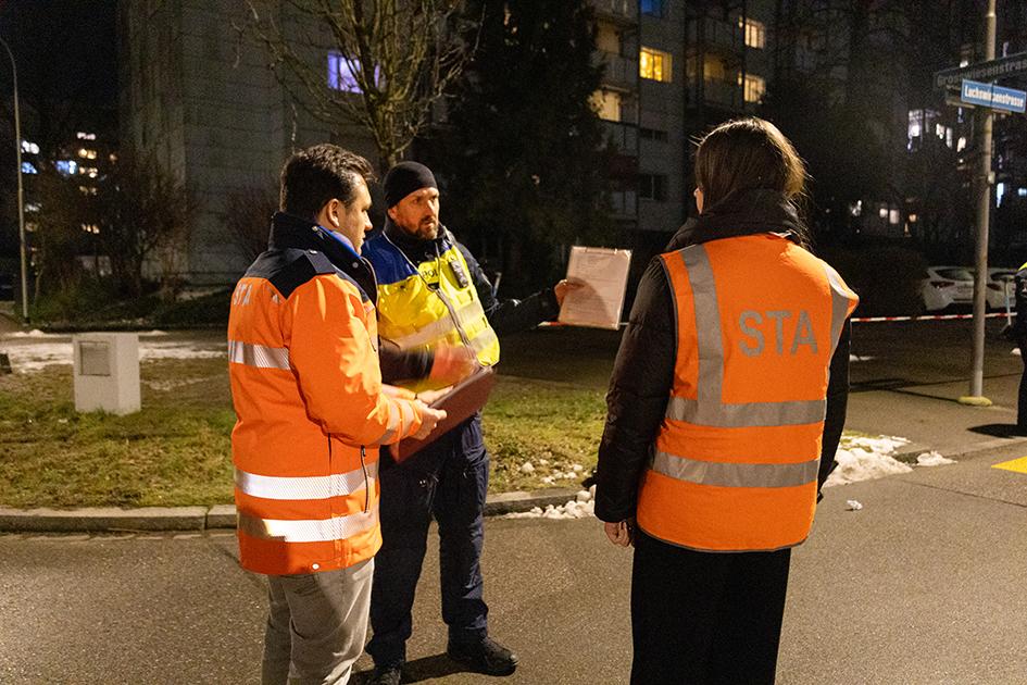 Drei Mitarbeitende von Staatsanwaltschaft und Polizei besprechen sich nachts an einem abgesperrten Einsatzort im Wohngebiet.