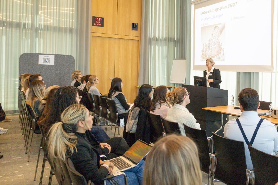 Grosses Sitzungszimmer mit Stuhlreihen und Personen, die von hinten aufgenommen wurden. Vorn spricht die Leitende Oberstaatsanwältin Susanne Leu.