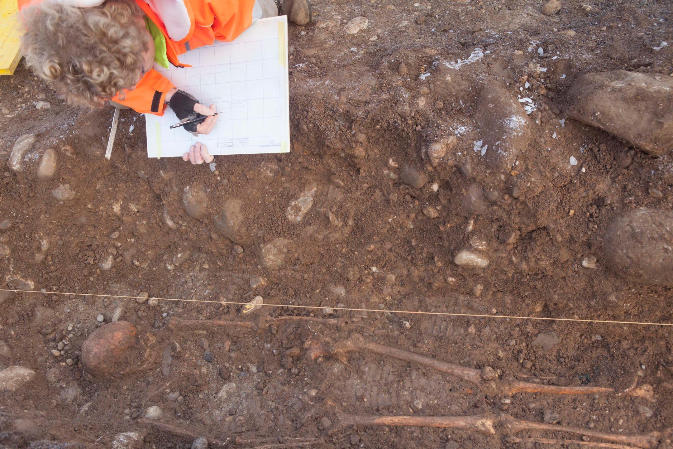 Eine Person erfasst menschliche Knochen auf einem Rasterplan auf einer archäologischen Grabung.