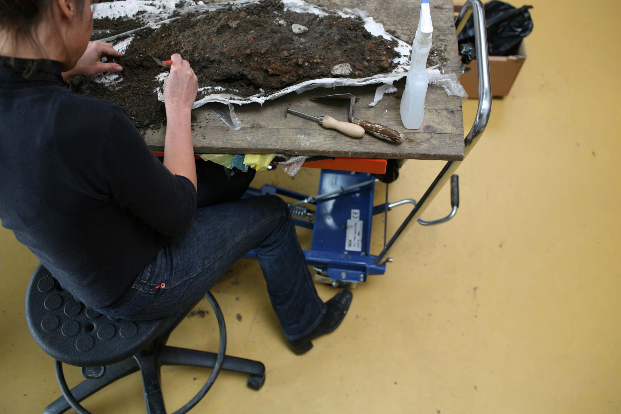Eine Frau untersucht einen Haufen Funde und Erde von einer Grabung im Labor.