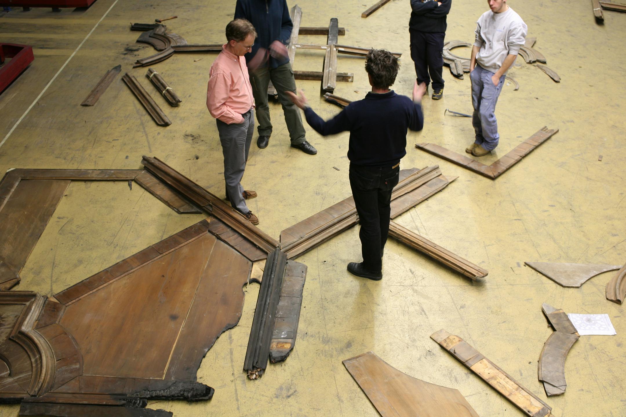 Eine Gruppe von fünf Personen beraten sich im Kreis. Auf dem Boden liegen Teile einer Holzdecke.