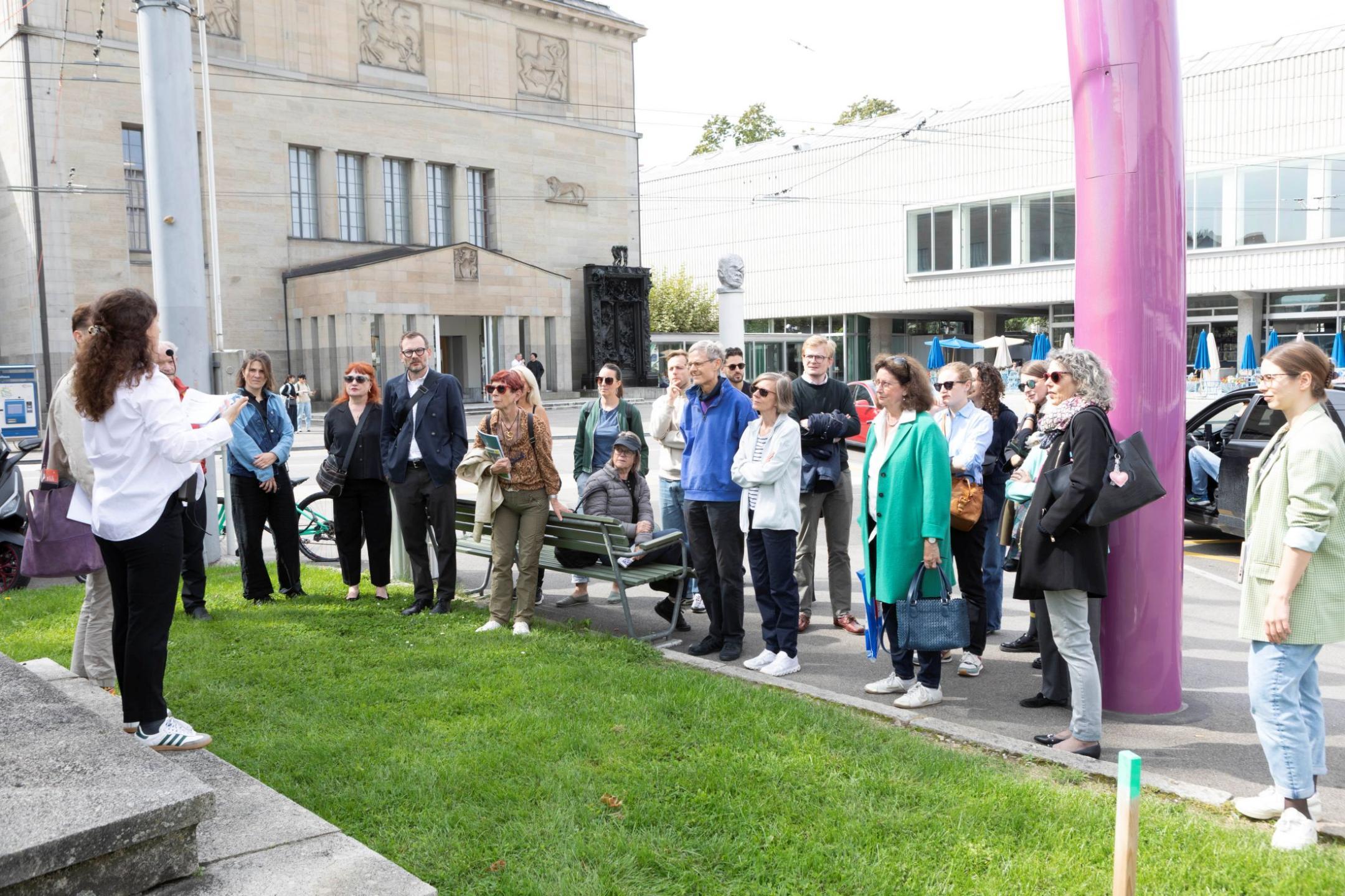 Eine Gruppe von Menschen lauschen auf dem Heimplatz den Ausführungen von Viviane. 