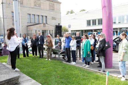 Eine Gruppe von Menschen lauschen auf dem Heimplatz den Ausführungen von Viviane. 