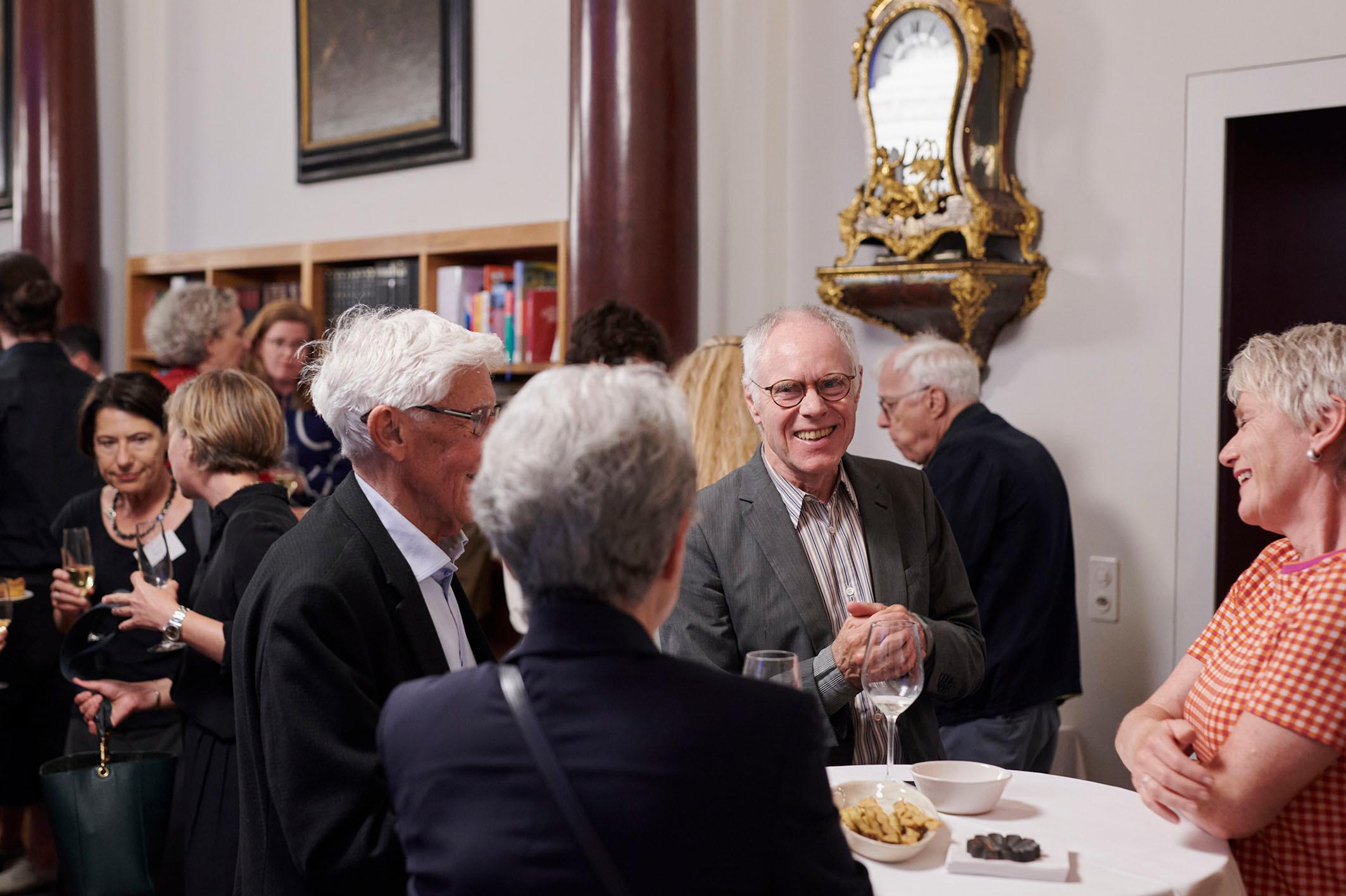Beatrice von Matt und ihr Mann stehen zusammen mit Regierungsrätin Jacqueline Fehr und Moritz Leuenberger, ehemaliger Bundespräsident, stehen um ein Tischchen und unterhalten sich. 