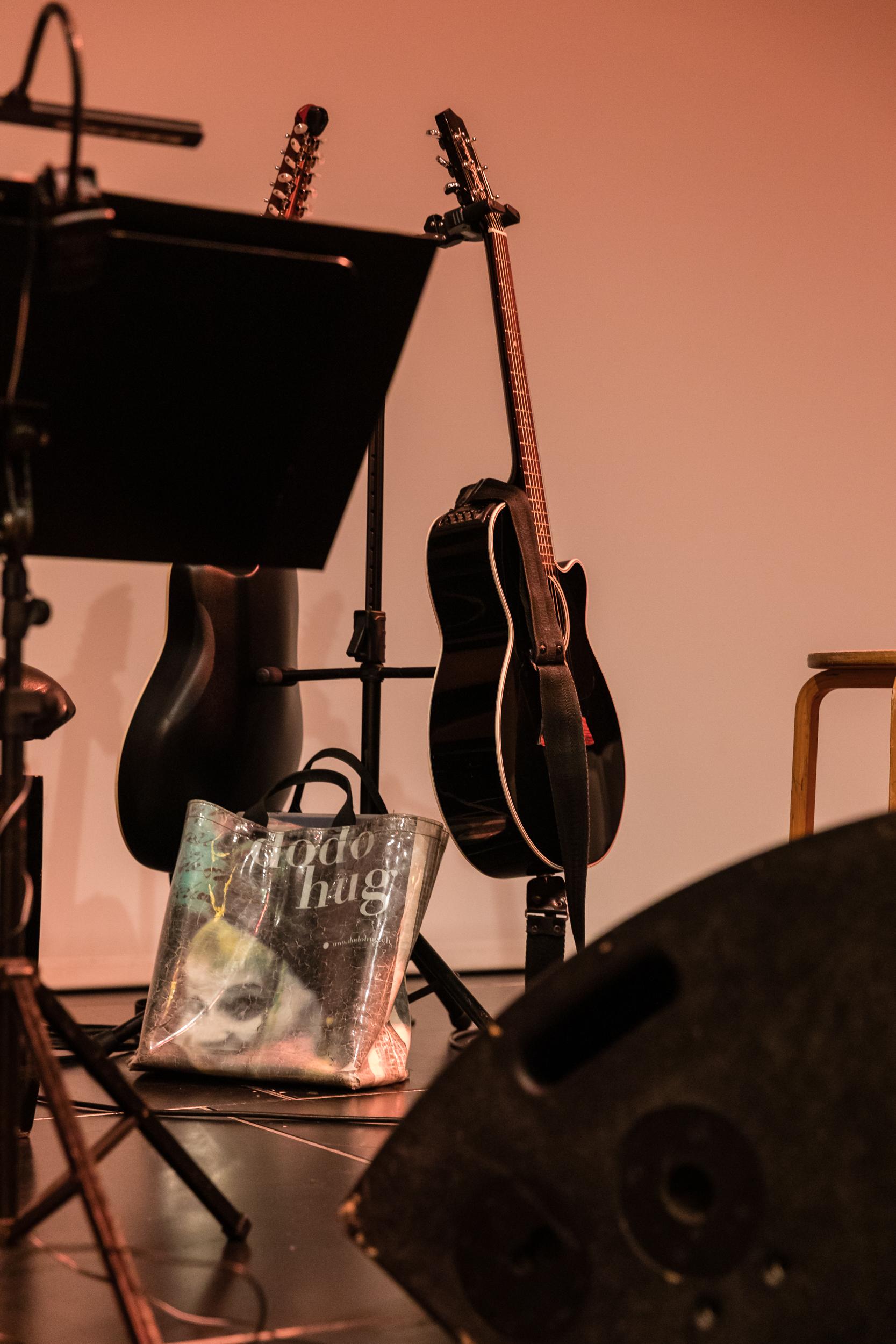 Ausschnitt der Bühne. Guitarre auf Ständer und Tasche mit Bild von Dodo Huge mit 