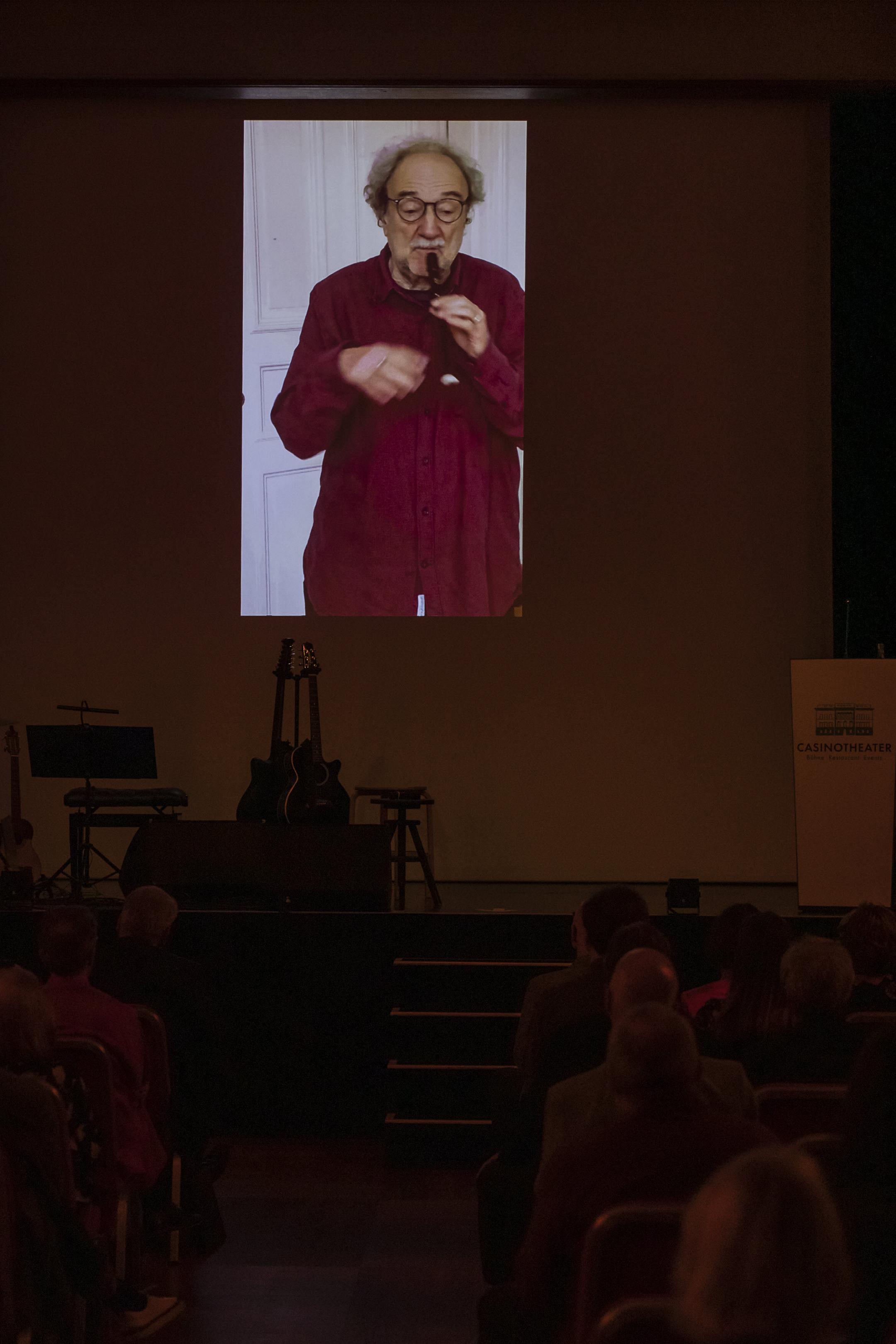 Christoph Marthaler mit Flöte auf der Leinwand übertragen