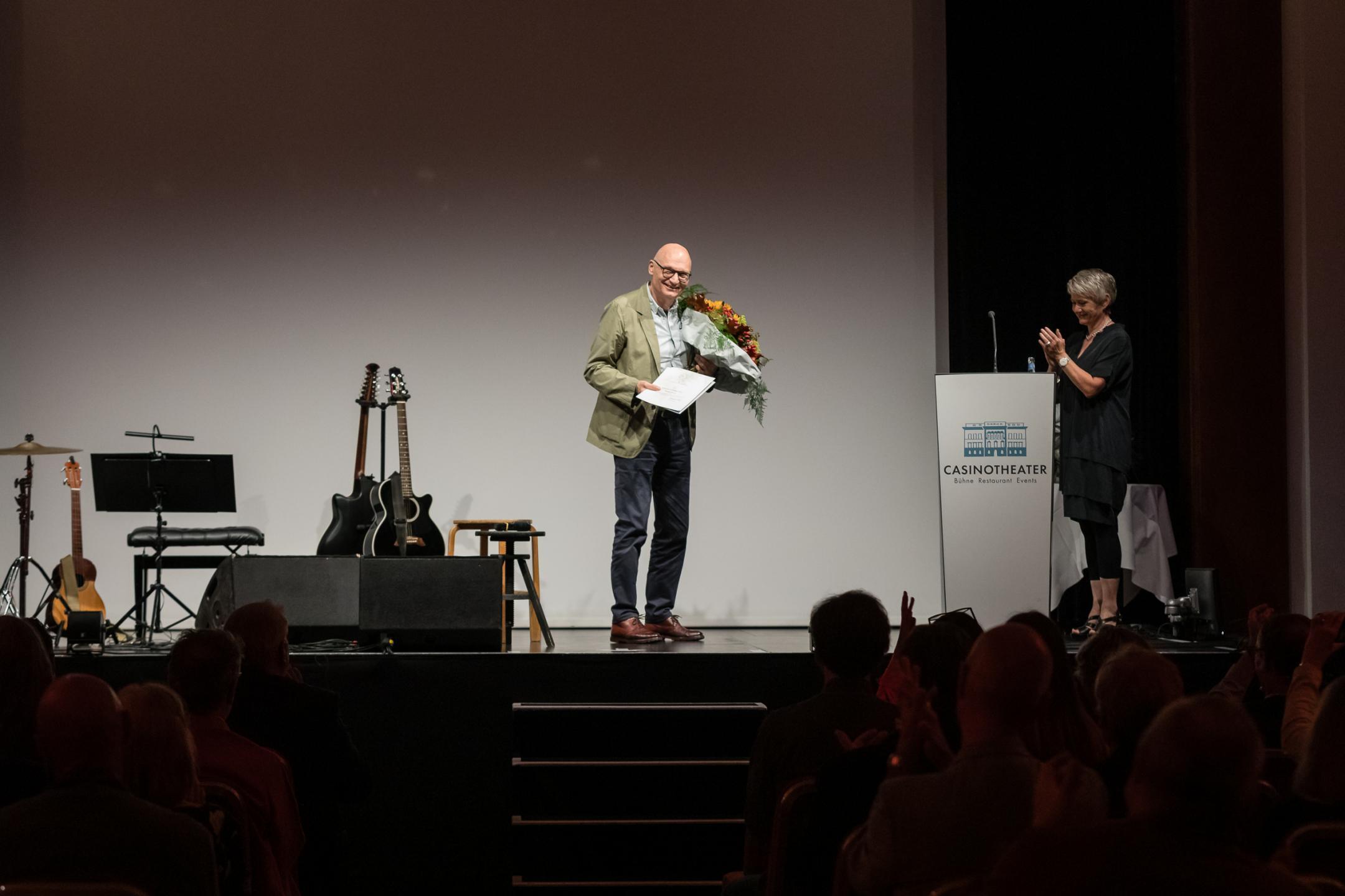 Christian Herdeg mit Blumenstrauss und Urkunde auf der Bühne
