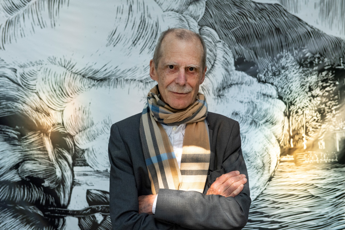 Portrait von Hannes Binder mit verschränkten Armen vor einer Wand mit Zeichnung