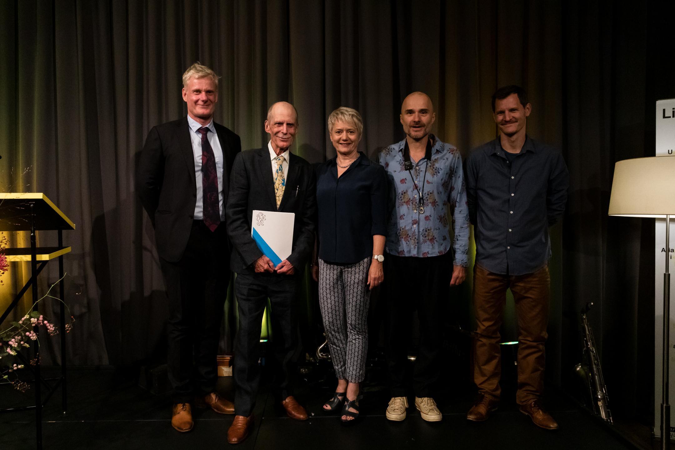 Gruppenbild auf der Bühne mit Dirk Vaihinger (Laudator), Hannes Binder (Preisträger), Jacquelline Fehr (Regierungsrätin), Marcel Lüscher und Mirco Häberli (Musiker)