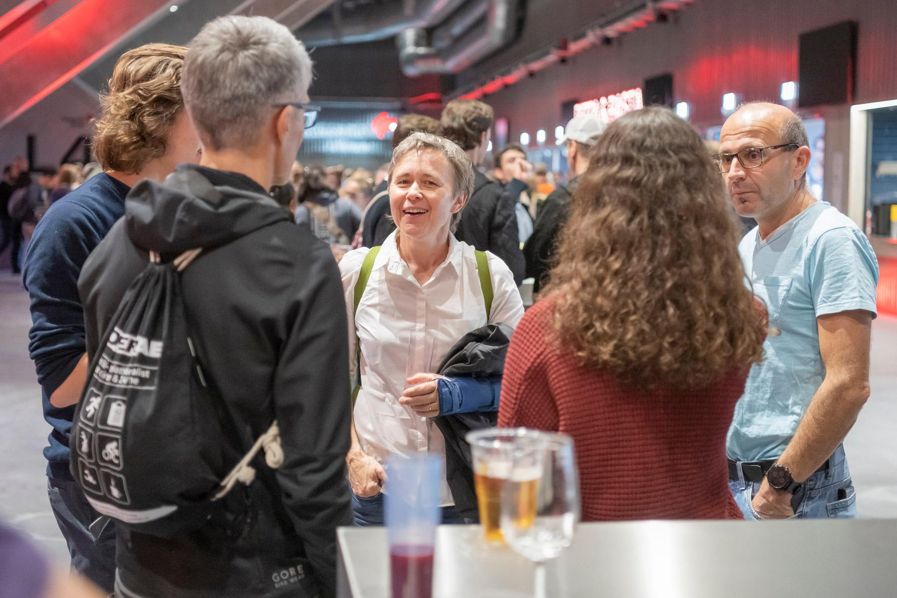 Fünf Personen stehen in einer Gruppe zusammen. Im Hintergrund sieht man viele weitere Personen,.