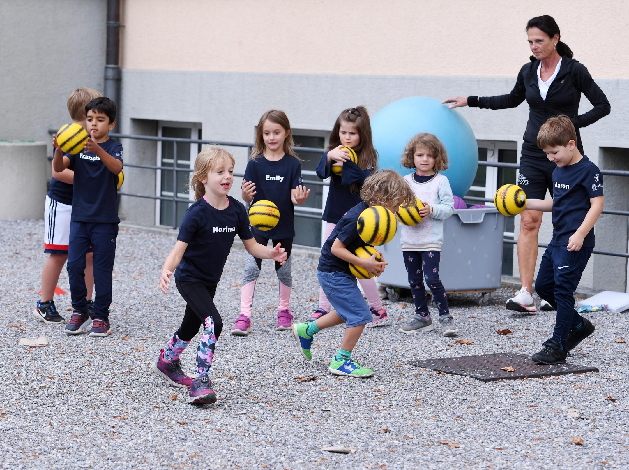 Mädchen und Knaben spielen draussen mit kleinen gelben Handbällen