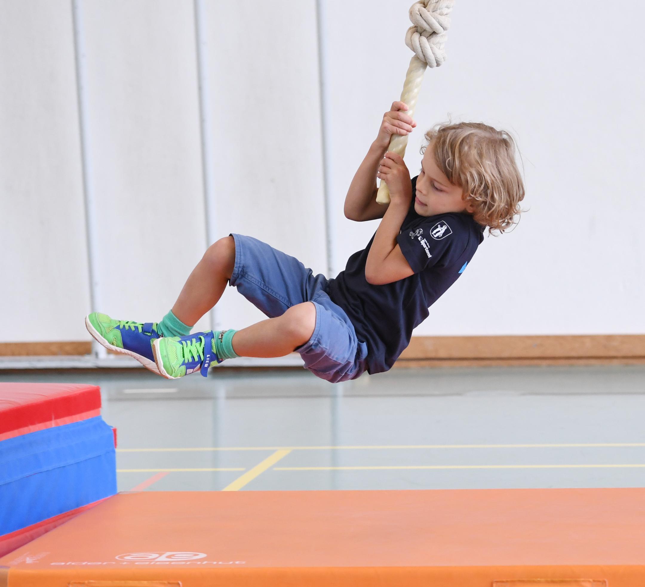 ein Knabe schwingt an einem Tau in der Turnhalle