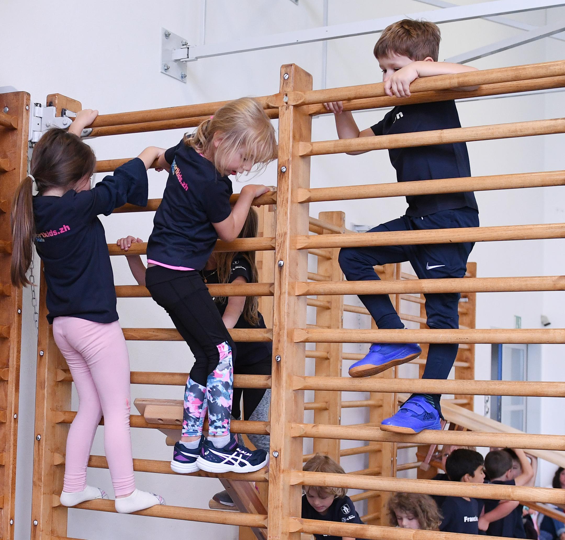 zwei Mädchen und ein Knabe klettern über eine Sprossenwand