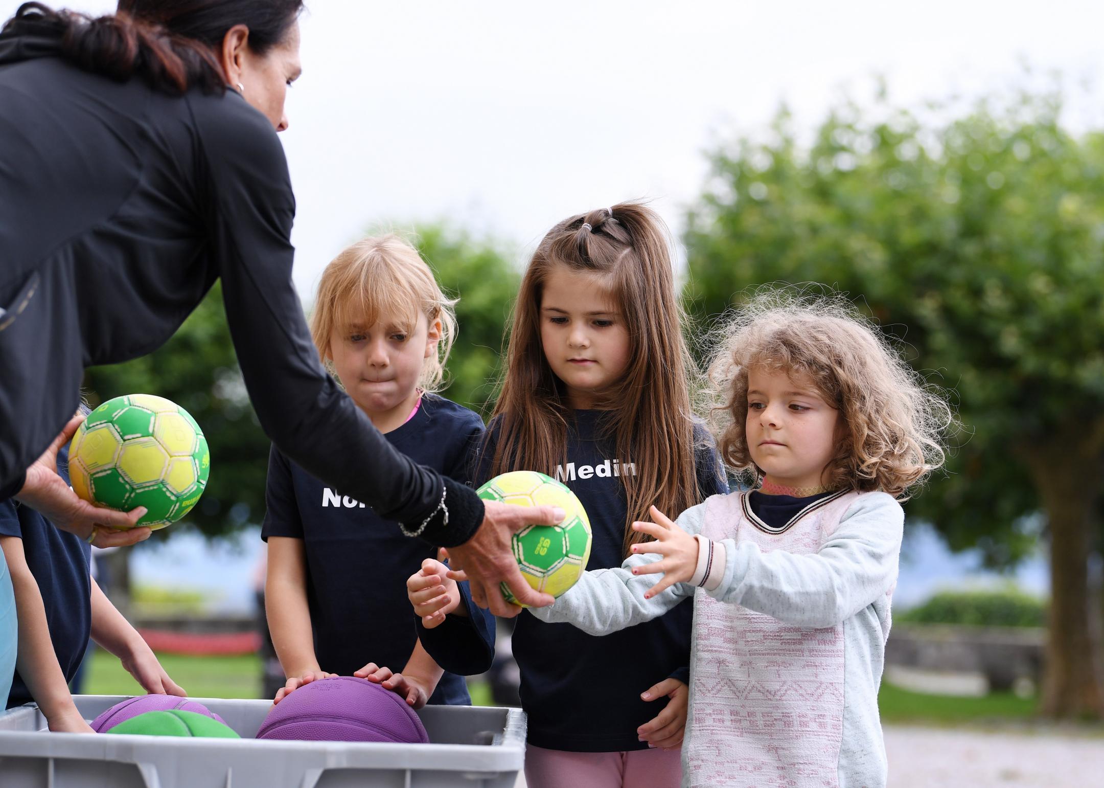 drei Mädchen erhalten von einer Trainerin je einen Handball