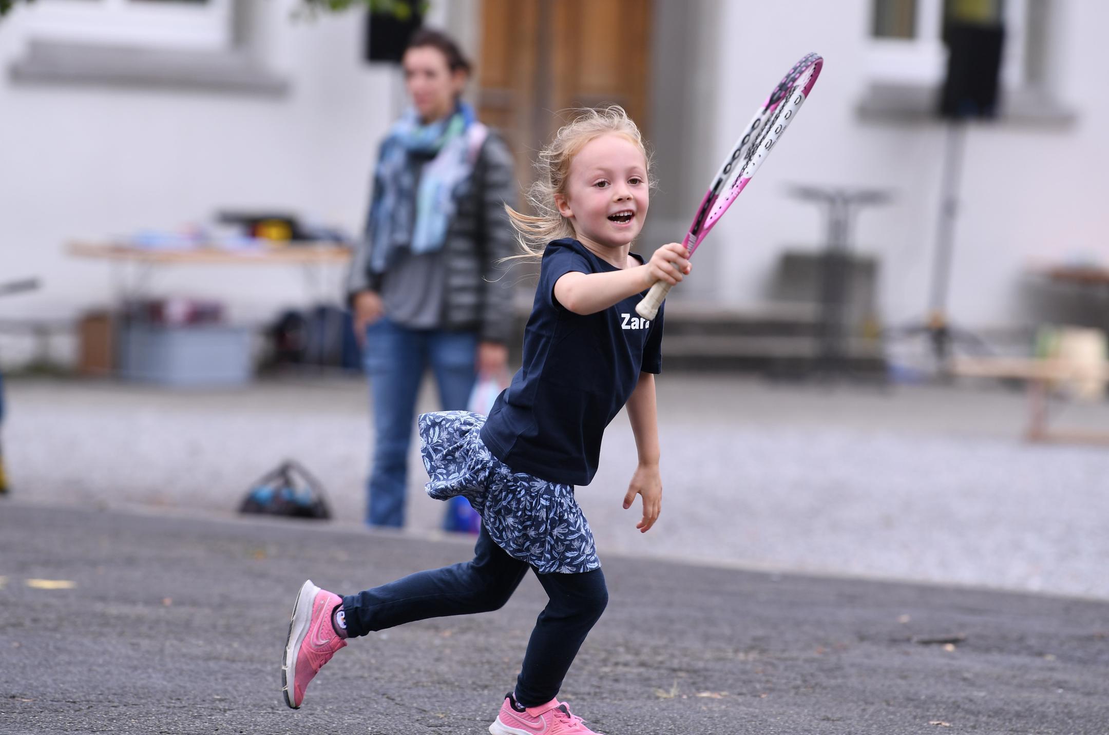 ein Mädchen mit Tennisschläger rennt auf dem Teerplatz 