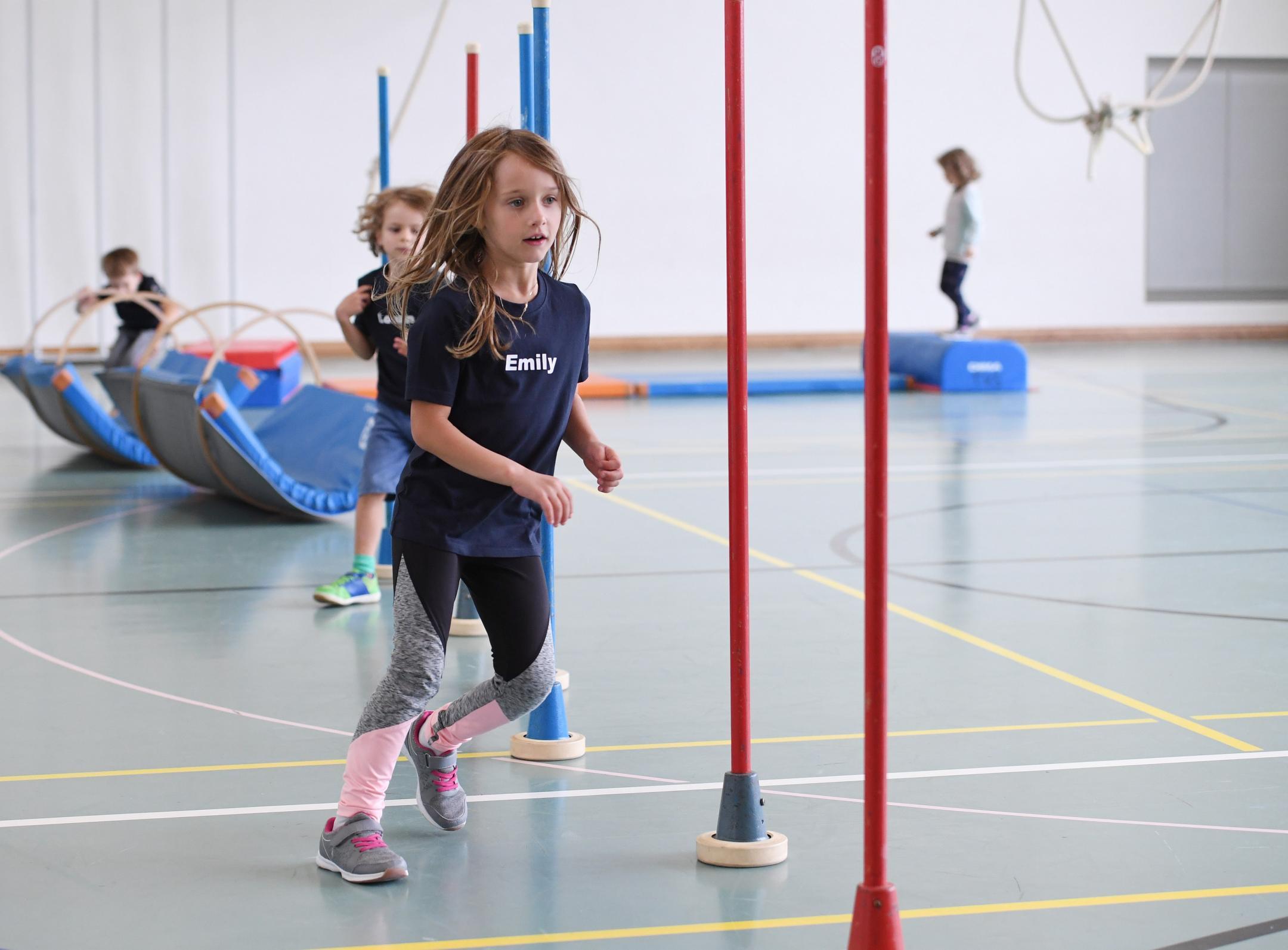 Mädchen rennen in einer Turnhalle um Malstäbe