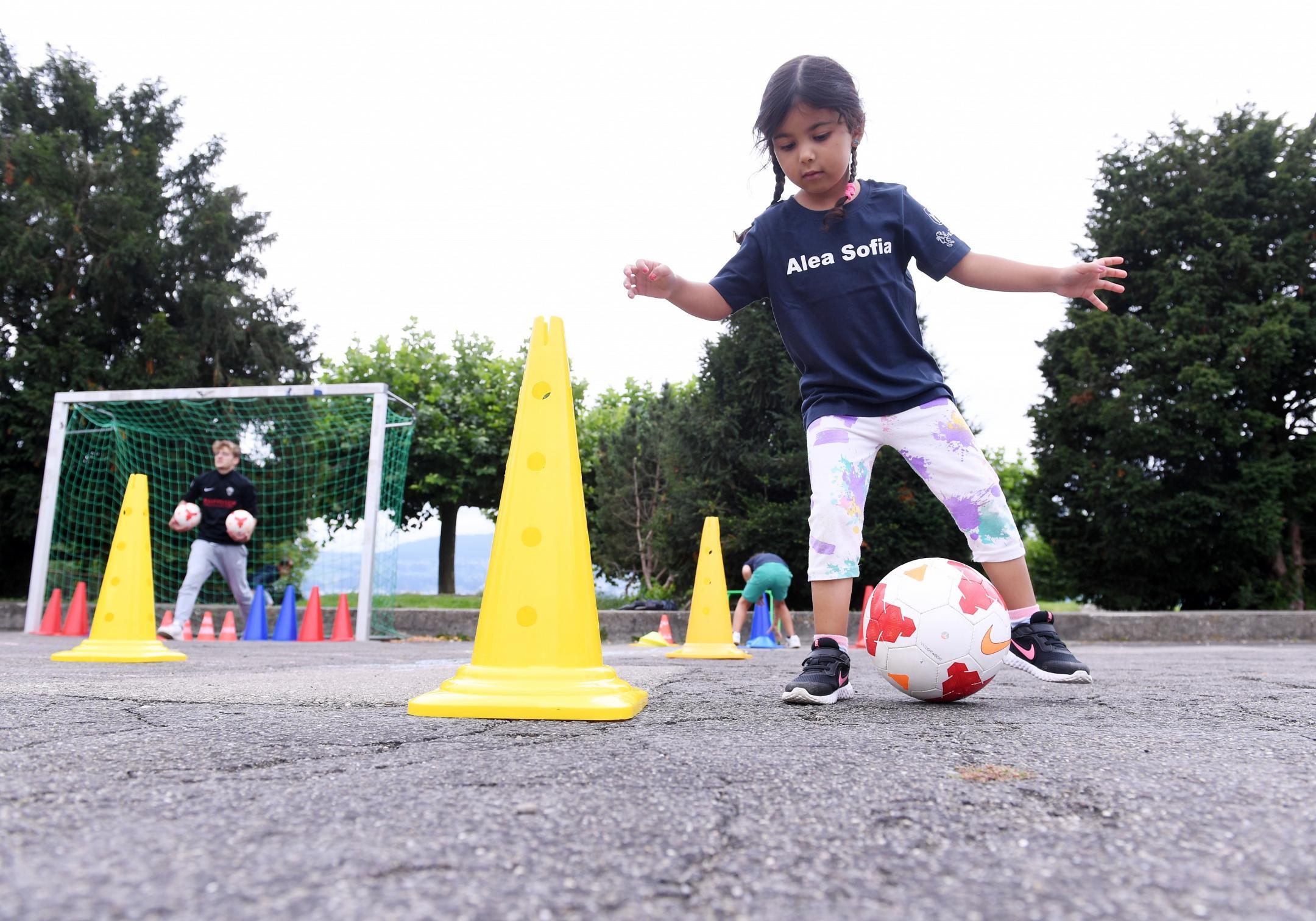 ein Mädchen dribbelt einen Fussball auf dem Pausenplatz um Pylonen