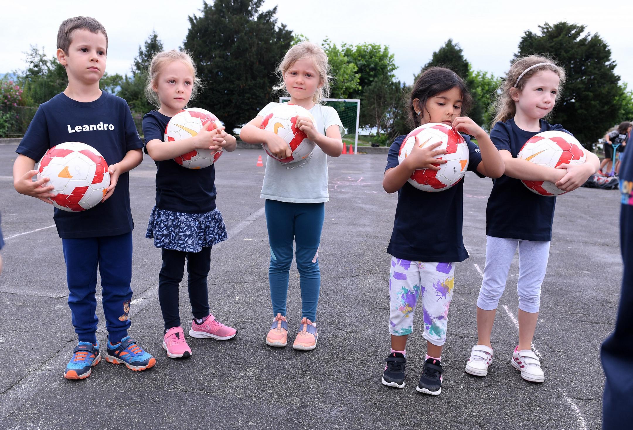 ein Knabe und vier Mädchen stehen auf dem Pausenplatz und halten einen Fussball in den Händen