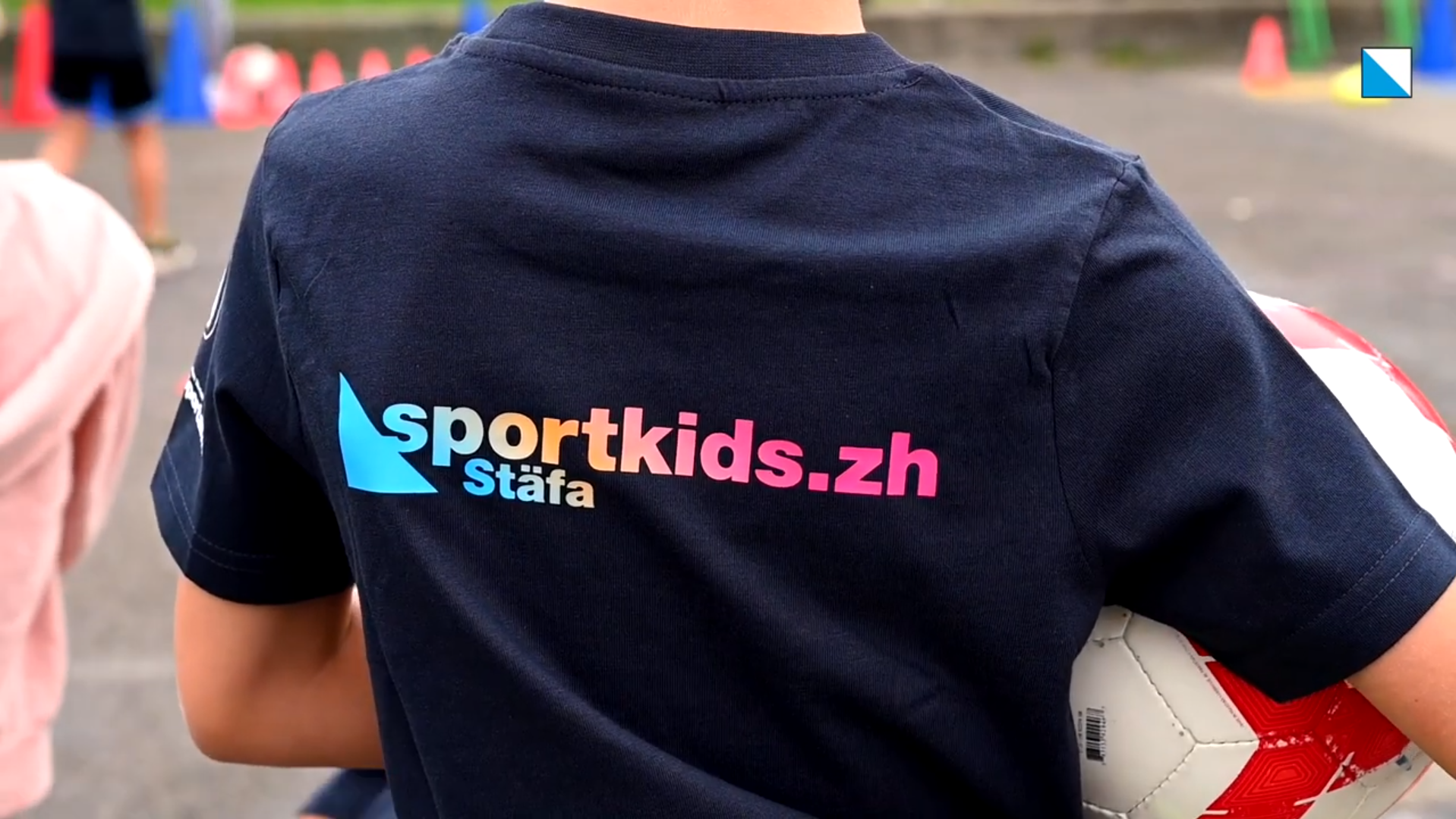 Nahaufnahme von Rücken von Kind mit Fussball unter dem Arm; auf T-Shirt ist sportkids.zh Stäfa aufgedruckt