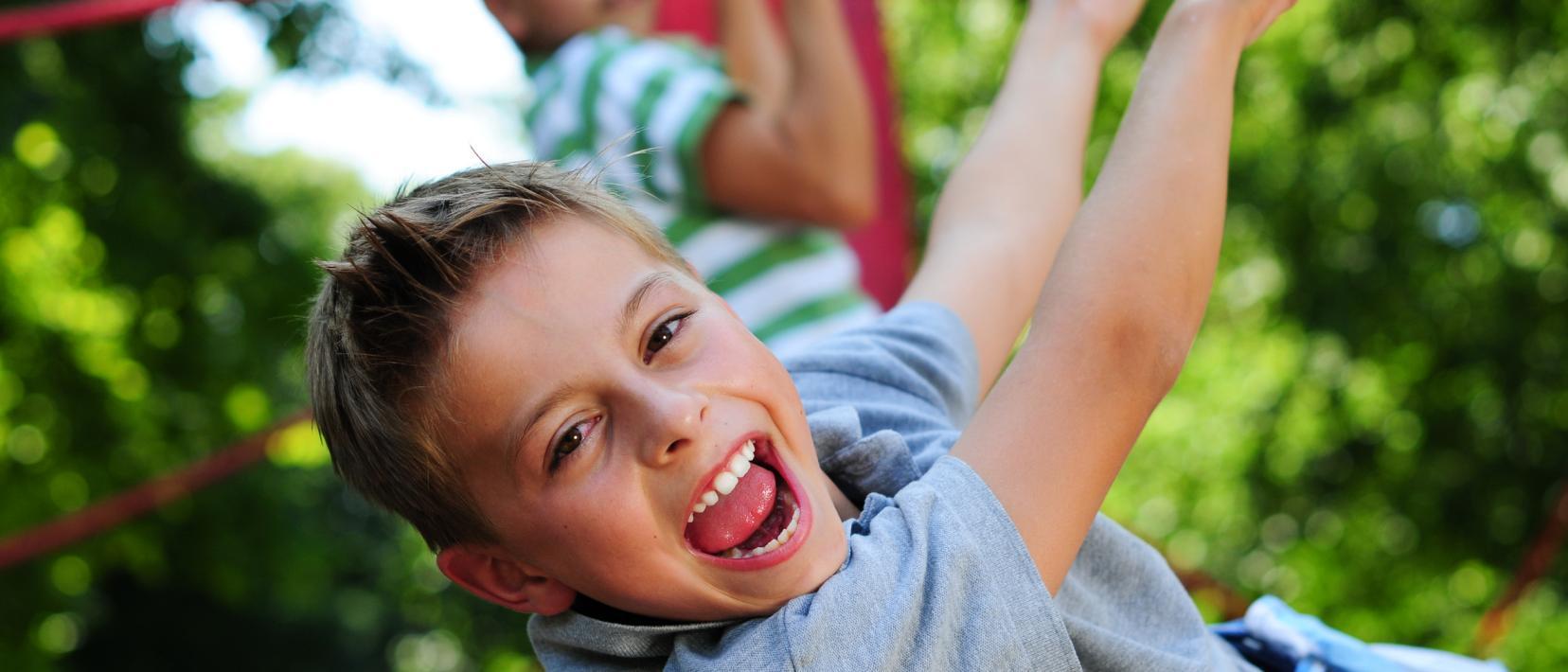 Zwei Knaben halten sich mit beiden Händen an einem roten Seil auf einem Spielplatz fest.