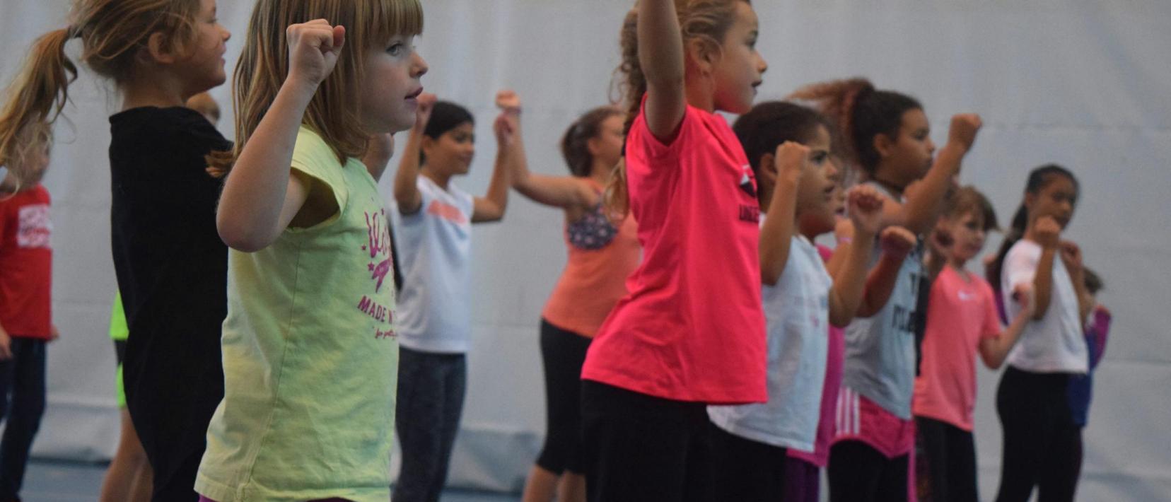 Eine Gruppe Primarschülerinnen übt in einer Turnhalle eine Tanzchoreo.