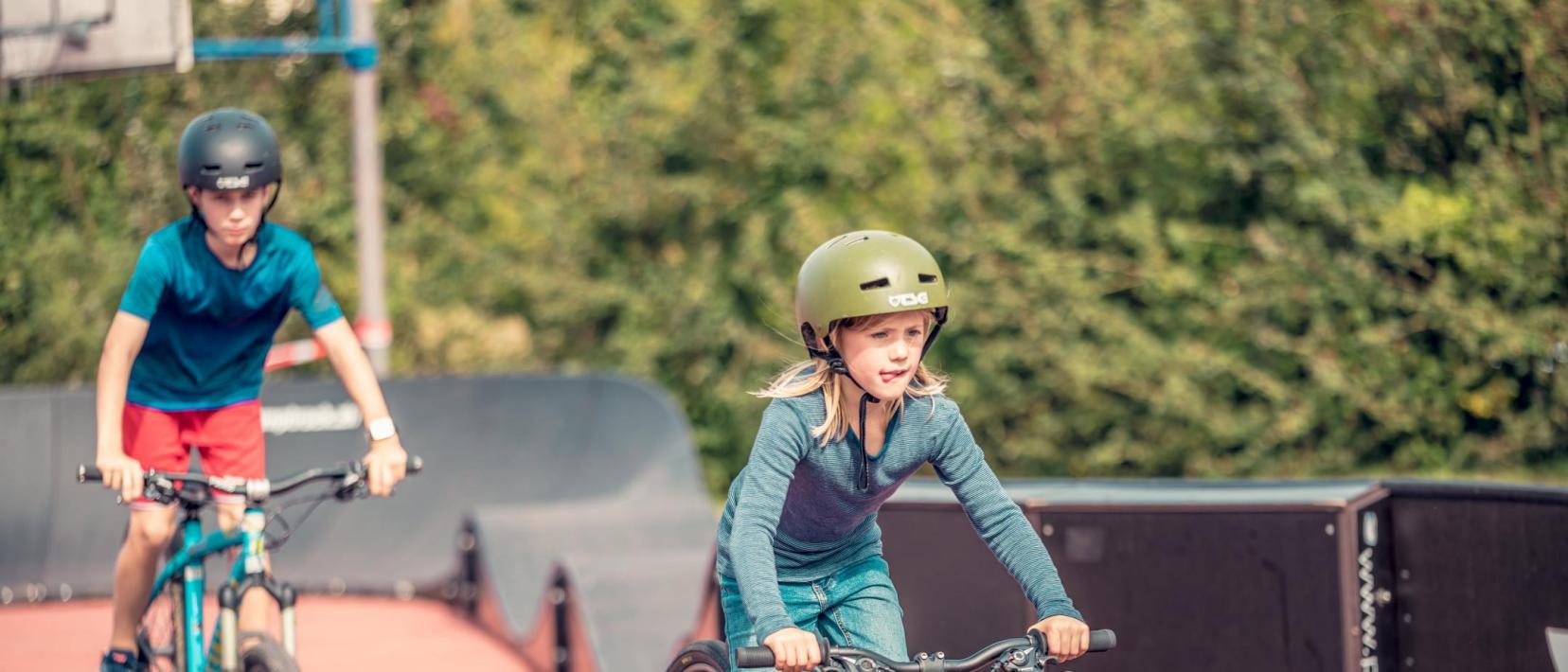 ein Mädchen und ein Knabe fahren mit dem Velo auf einem mobilen Pumptrack, einem Rundkurs mit Wellen und Kurven