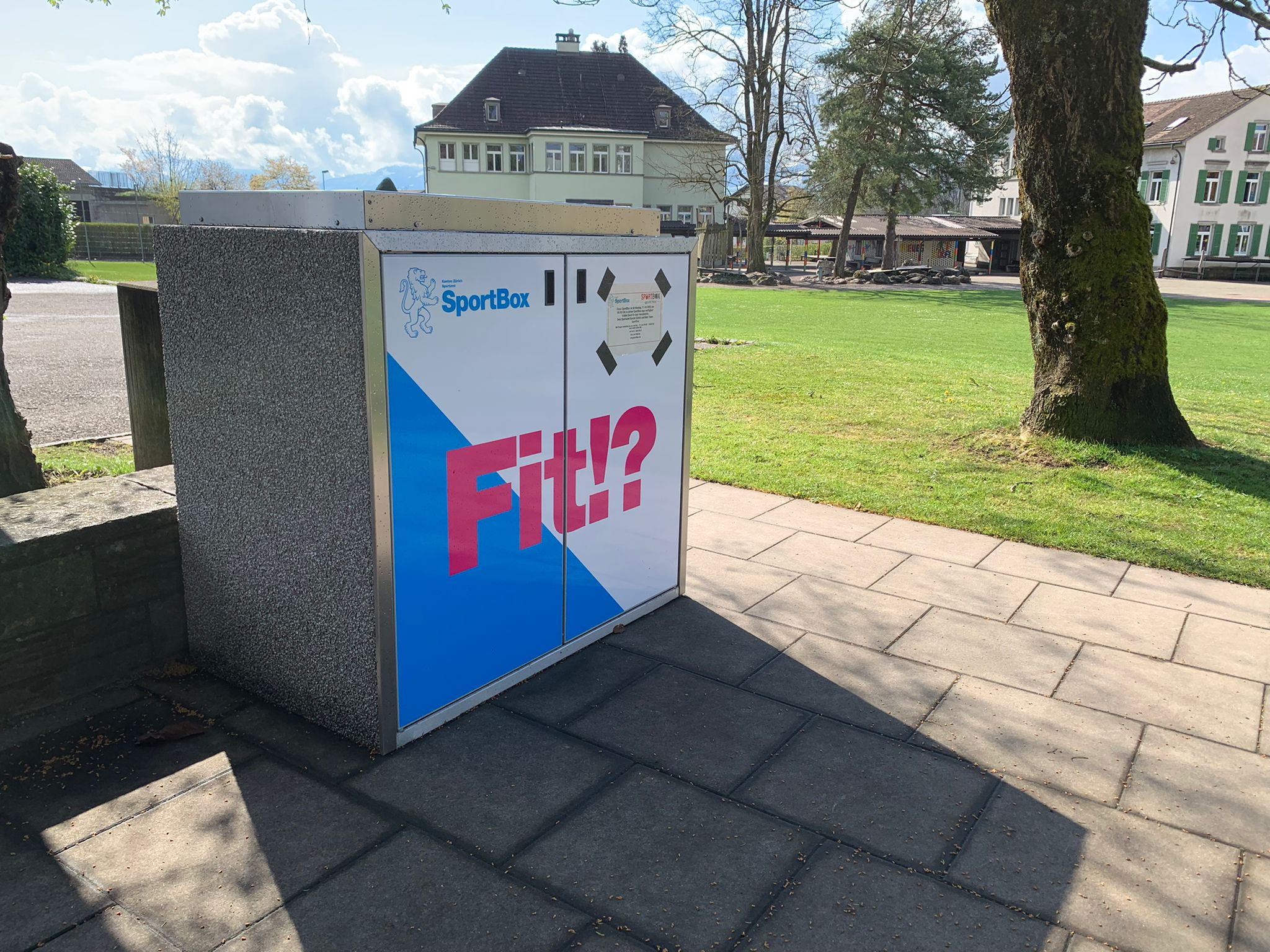 Eine SportBox (Verleihsystem mit Sport- und Fitnessequipment) steht bei einer Wiese in Hombrechtikon