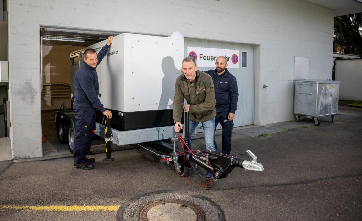 Drei Männer schieben ein Notstromaggregat in ein Gebäude der Feuerwehr. 