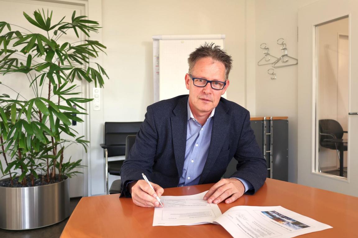 Christoph Zemp, der Amtschef des AWEL, sitzt im Anzug in seinem Büro am Schreibtisch  auf dem verschiedene Unterlagen liegen.
