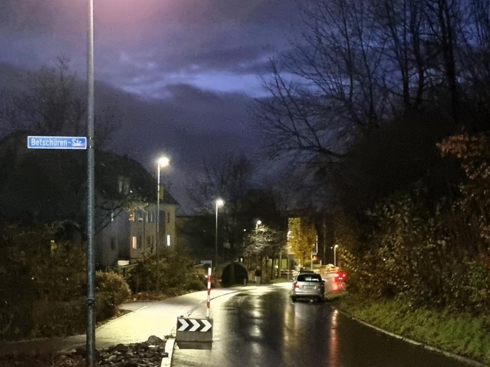 Eine Strasselaterne beleuchtet in dunkler Nacht eine regennasse Strasse. 