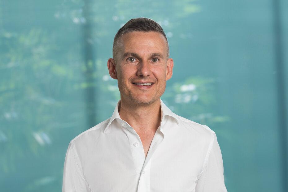 Portrait von Rainer Schöne, Mitglied der Geschäftsleitung bei Energie 360°. Er lächelt, trägt ein weisses Hemd und steht vor einer hellblauen Wand.